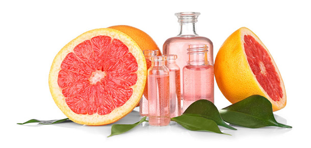 Aufgeschnittene Grapefruit liegt neben einigen rosa farbenen Grapefruit-Öl-Fläschchen. 